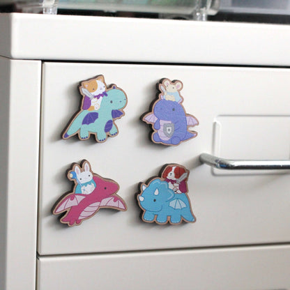 Four wooden magnets of a cute animal riding on top of a colorful dragon on a white drawer