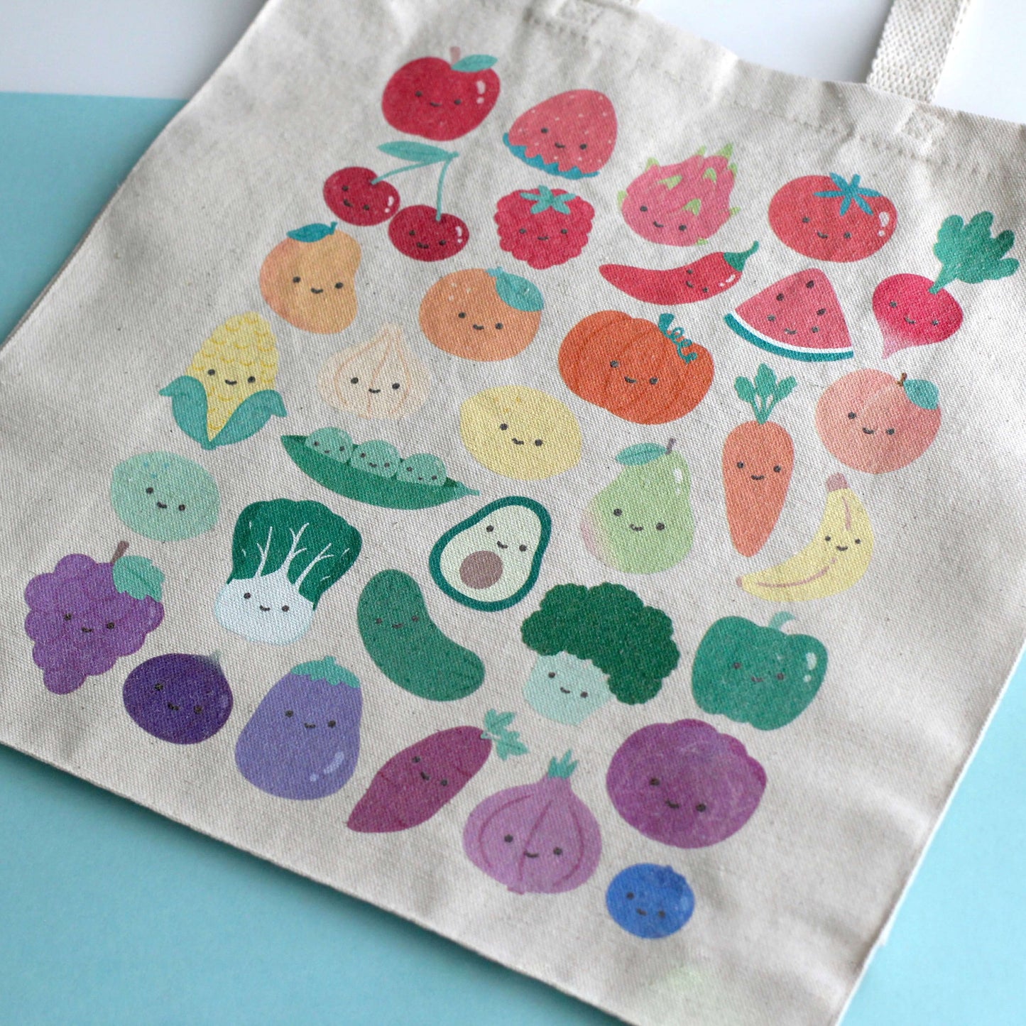 Close up of a tote bag with print of colorful fruits and vegetables with smiling faces. 