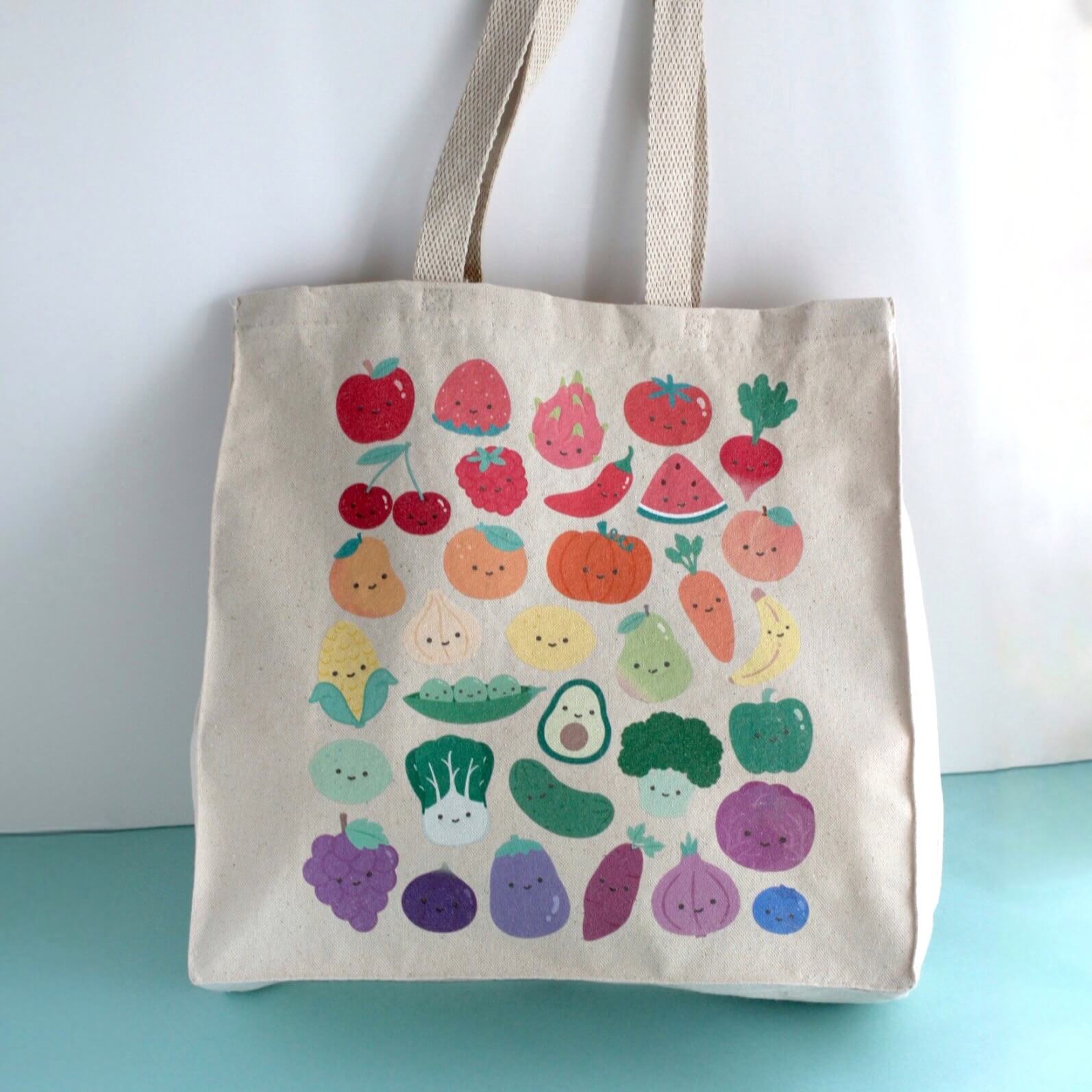 Tote bag with colorful fruit and vegetable pattern on a light blue surface.